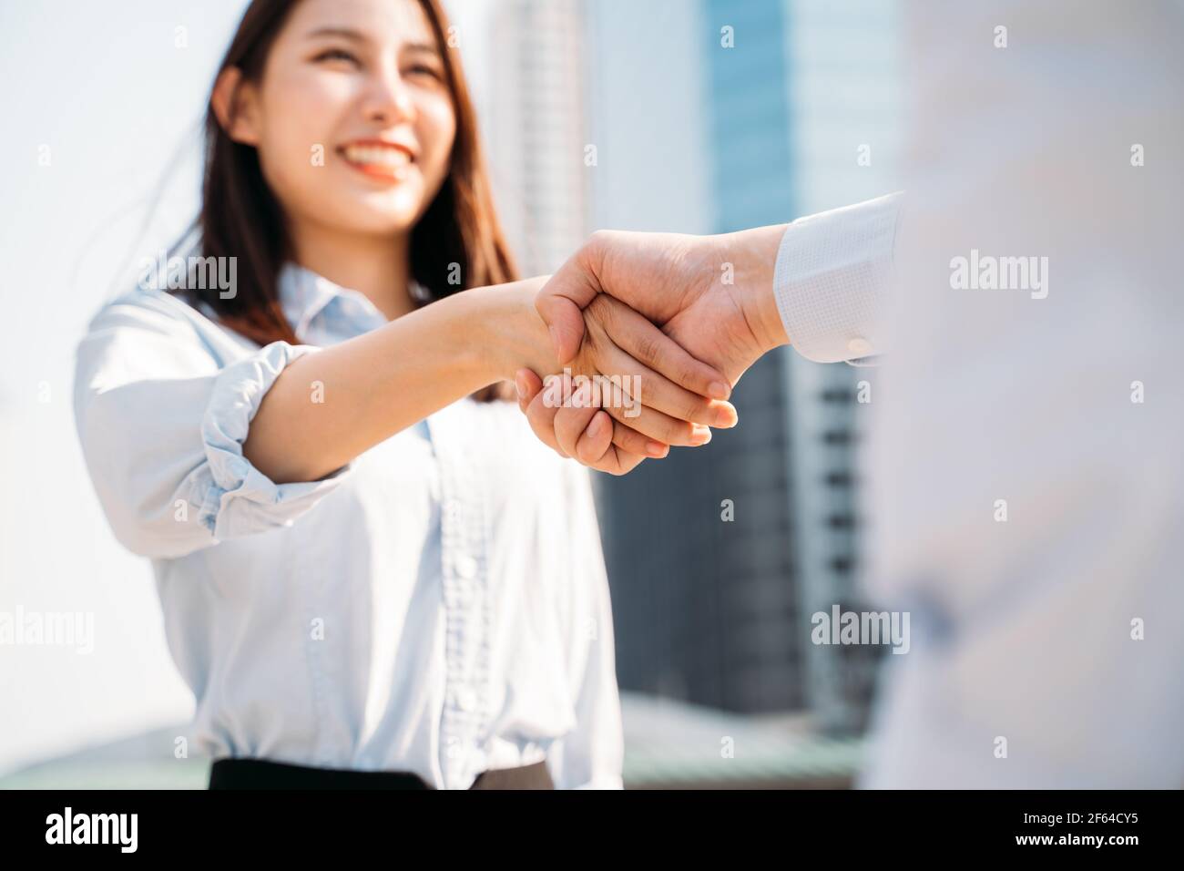 Closeup di mani di sorridente giovane donna d'affari asiatica scuotendo le mani con un uomo d'affari in città mentre incontrando il manager per l'intervista Foto Stock