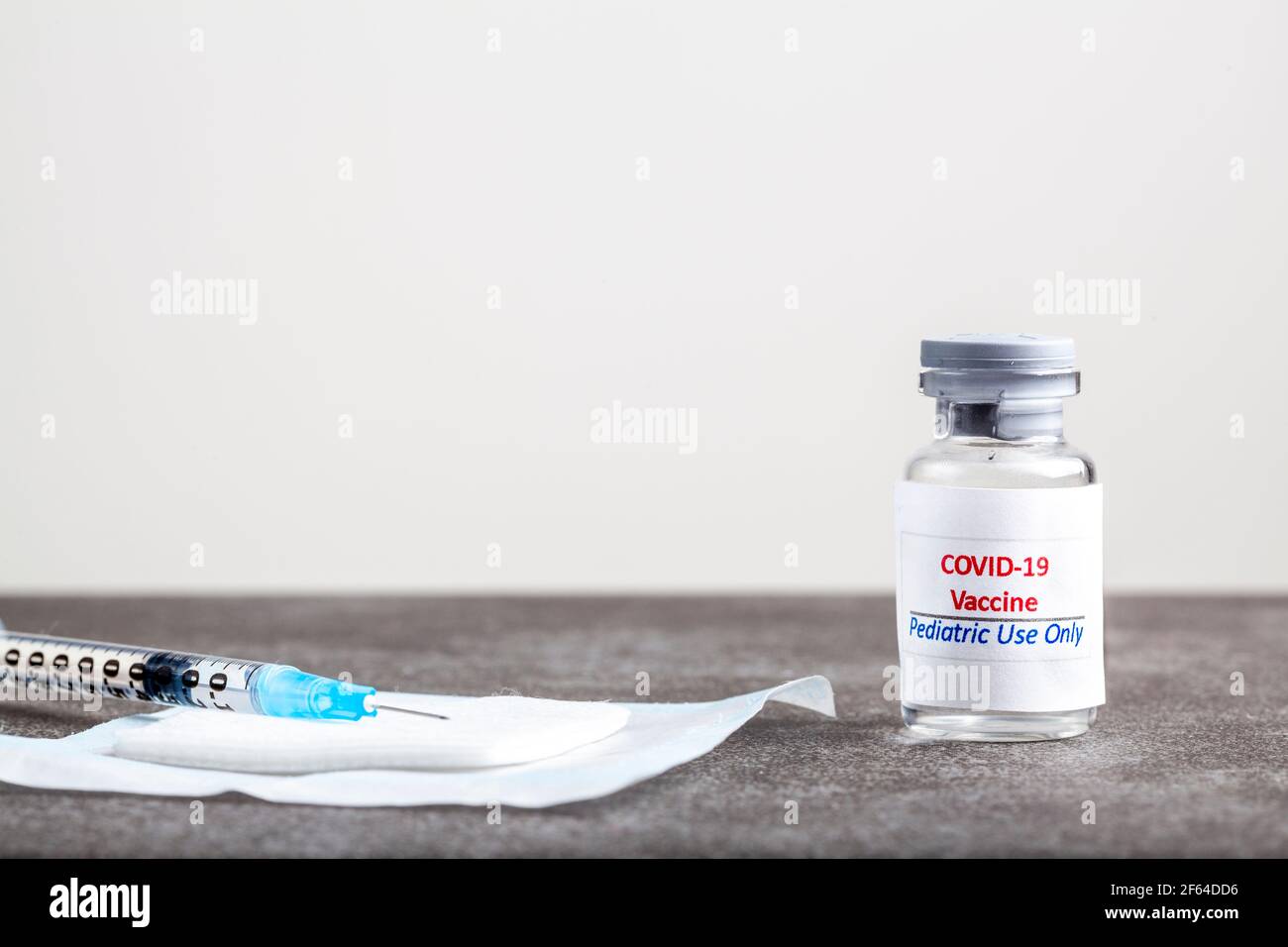 Immagine concettuale che mostra il vaccino COVID 19 progettato per l'uso pediatrico solo in un flaconcino di vetro con un ago e una siringa riempito con il vaccino prima della cenere Foto Stock