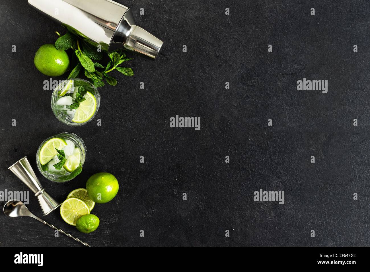 Ingredienti e utensili da bar per preparare un cocktail mojito con cubetti di ghiaccio, menta fresca e lime su sfondo nero. Set di accessori per barre per mojito coc Foto Stock