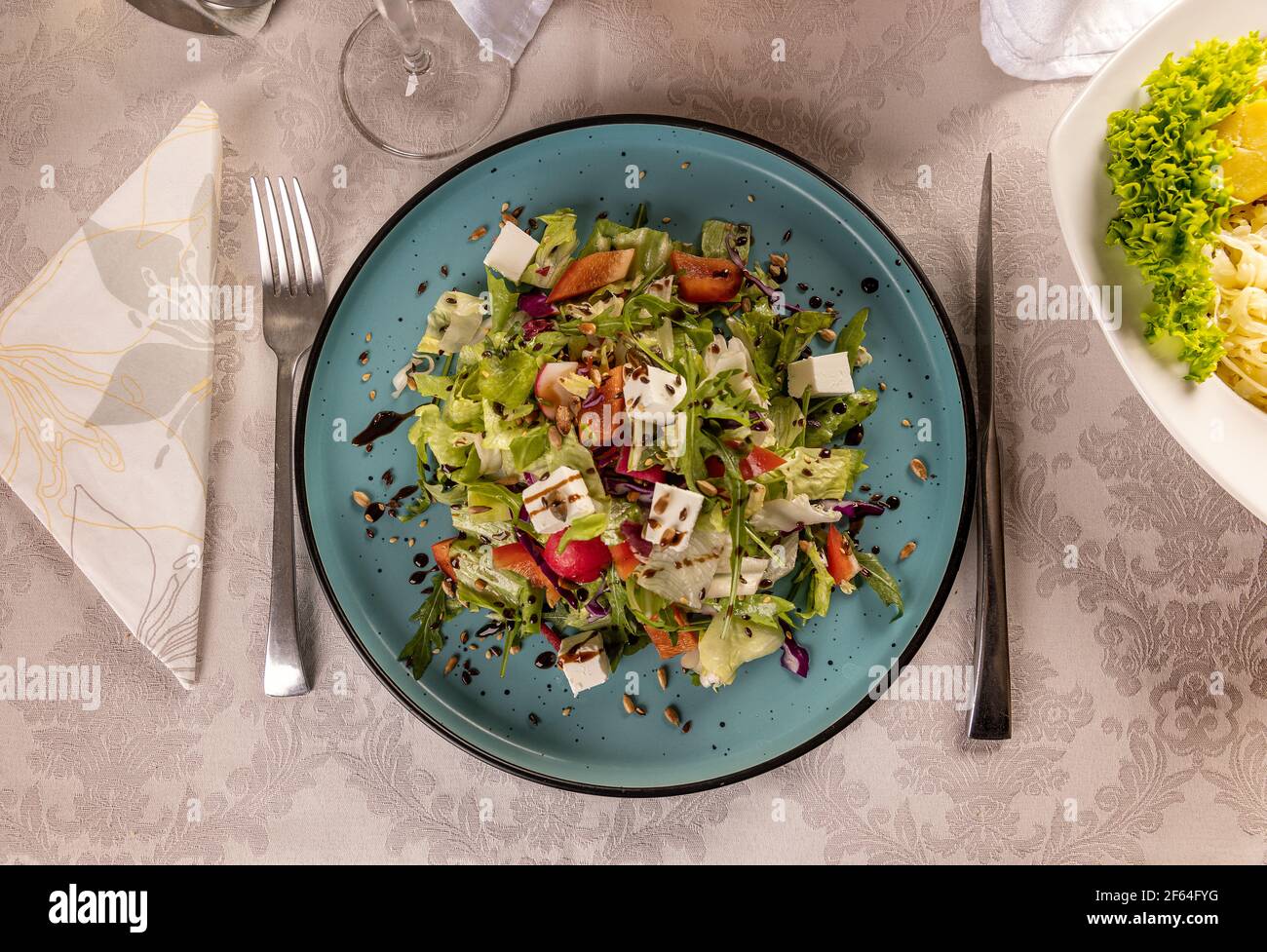 Pranzo con dieta colorata, insalata di primavera. Foglie fresche, rafano, formaggio feta e olio d'oliva in un piatto blu Foto Stock