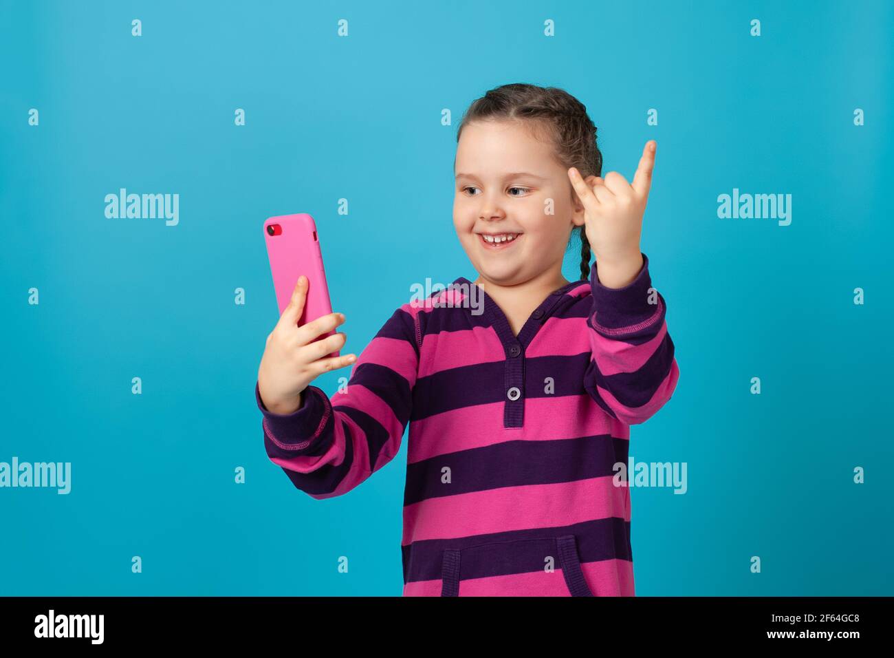 primo piano ritratto di una ragazza ridente con i pigtail che parlano in videochiamata, tenendo il telefono a braccio e mostrando segni di corna con le dita Foto Stock