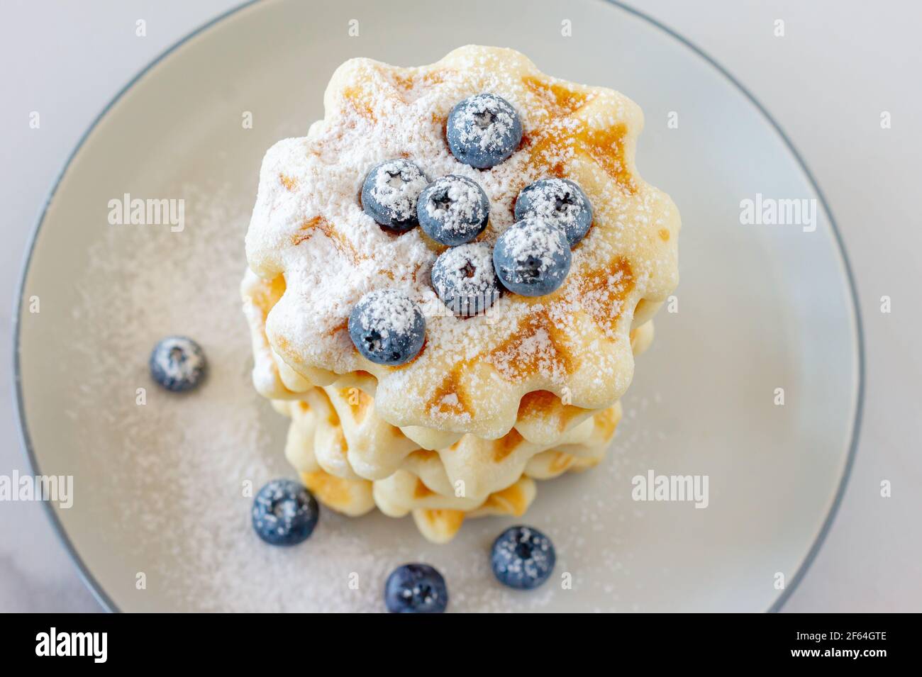 Waffle fatti in casa alla vaniglia con polvere di zucchero e mirtilli di cenere su un piatto, colazione perfetta per tutta la famiglia. Foto Stock