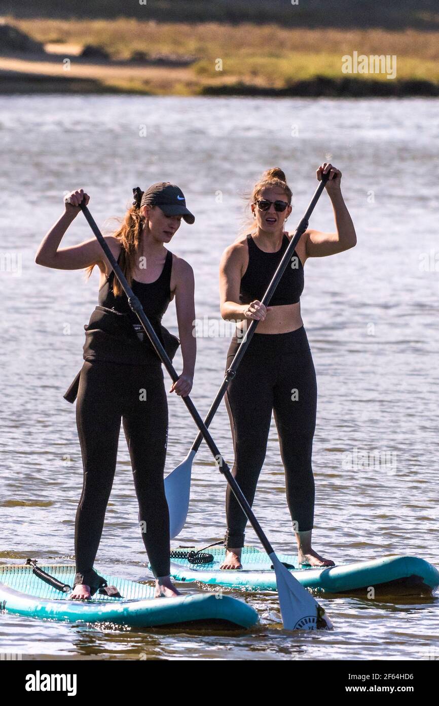 Due vacanzieri donne in piedi su Paddleboards Stand Up e pagaiando sul fiume Gannel a Newquay in Cornovaglia. Foto Stock
