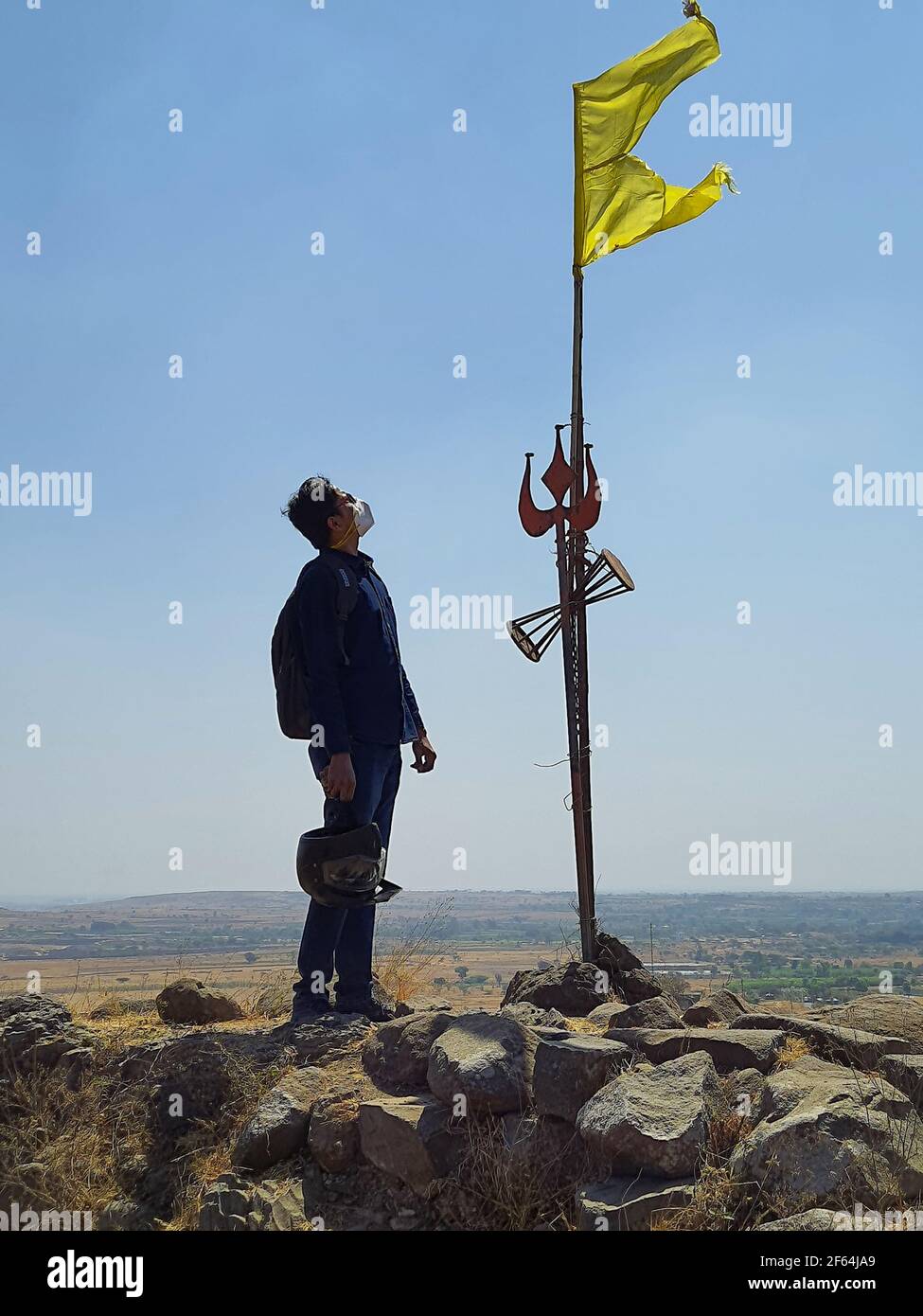 Uomo che guarda la bandiera gialla indù e Trishula situato sopra massa alta Foto Stock