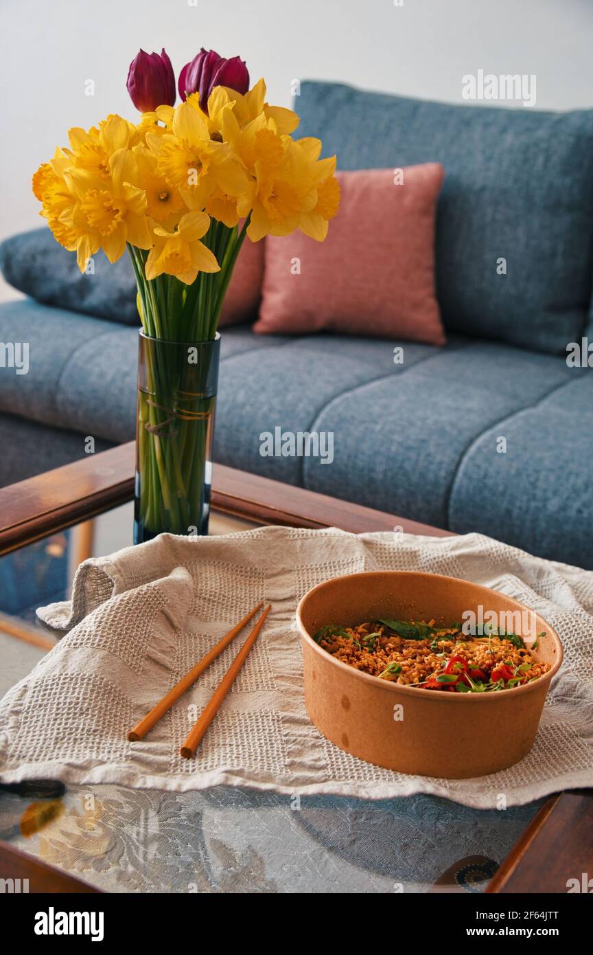 Piatti asiatici da asporto con bastoncini di pollo sul tavolo decorato con fiori in vaso Foto Stock