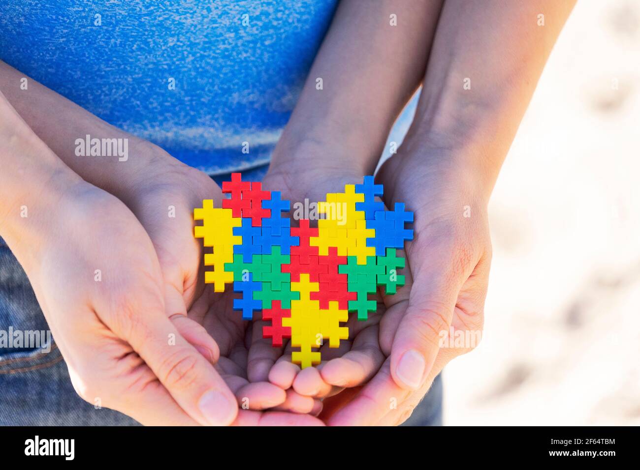 Mani autistiche di capretto supportate da madre che tiene il cuore multicolore del puzzle. Concetto di giorno di consapevolezza autismo mondiale Foto Stock