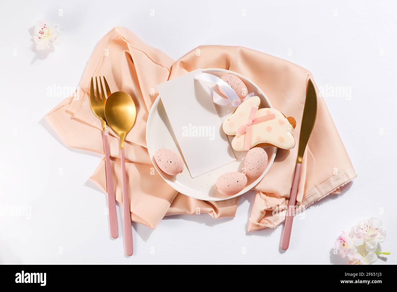 Tavolo di Pasqua con uova, biscotti conigliati, piatto, posate e fiori bellissimi con menu Foto Stock