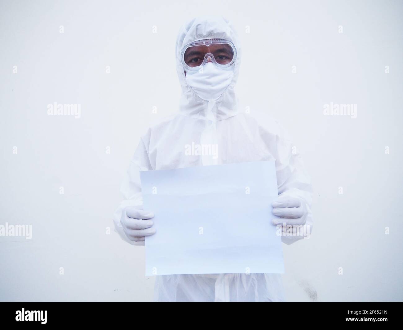 Giovane medico o scienziato in uniforme DPI suite tenendo carta bianca per il testo con entrambe le mani mentre si guarda avanti. Coronavirus o COVID-19 concept isola Foto Stock