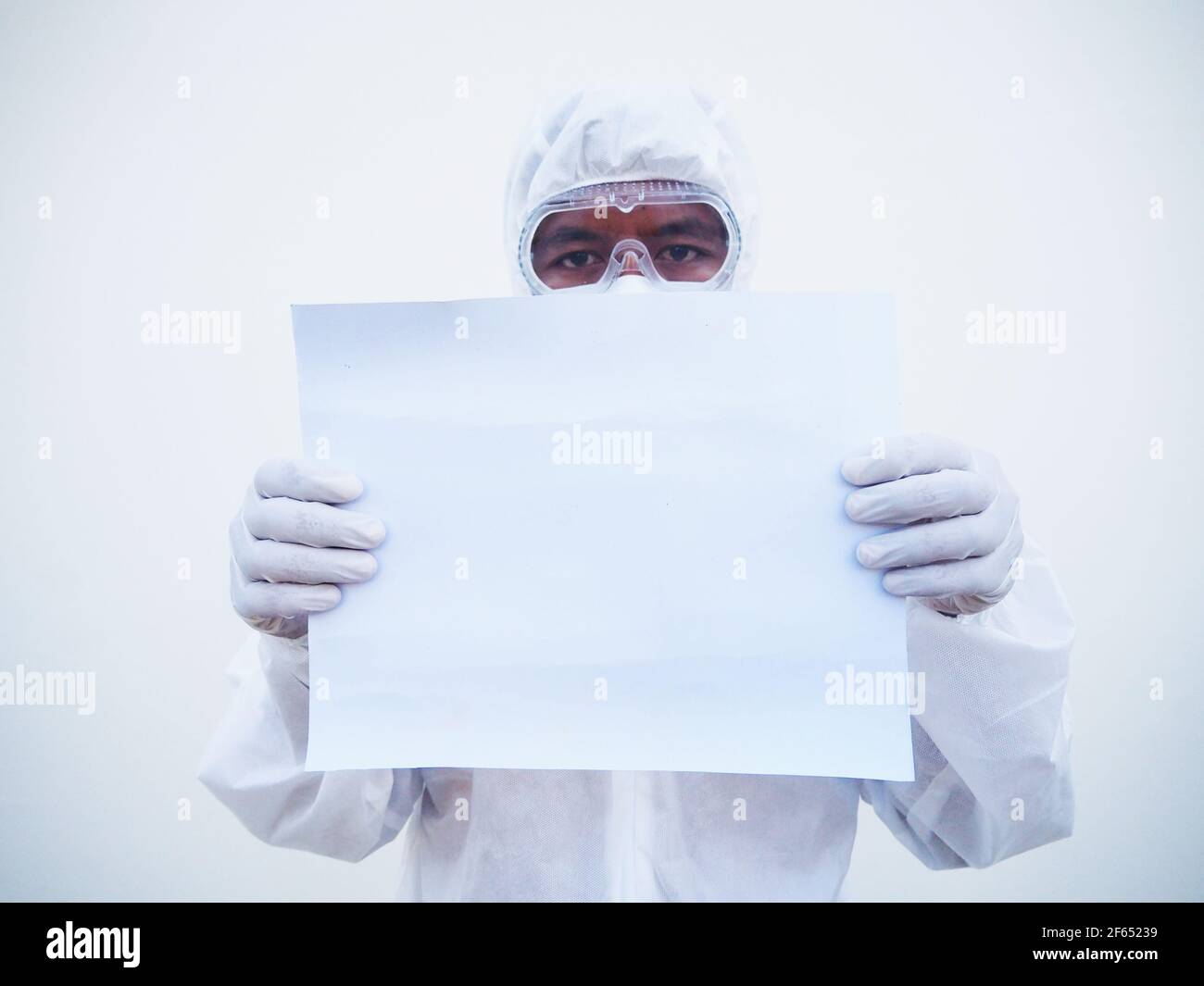 Giovane medico o scienziato in uniforme DPI suite tenendo carta bianca per il testo con entrambe le mani mentre si guarda avanti. Coronavirus o COVID-19 concept isola Foto Stock