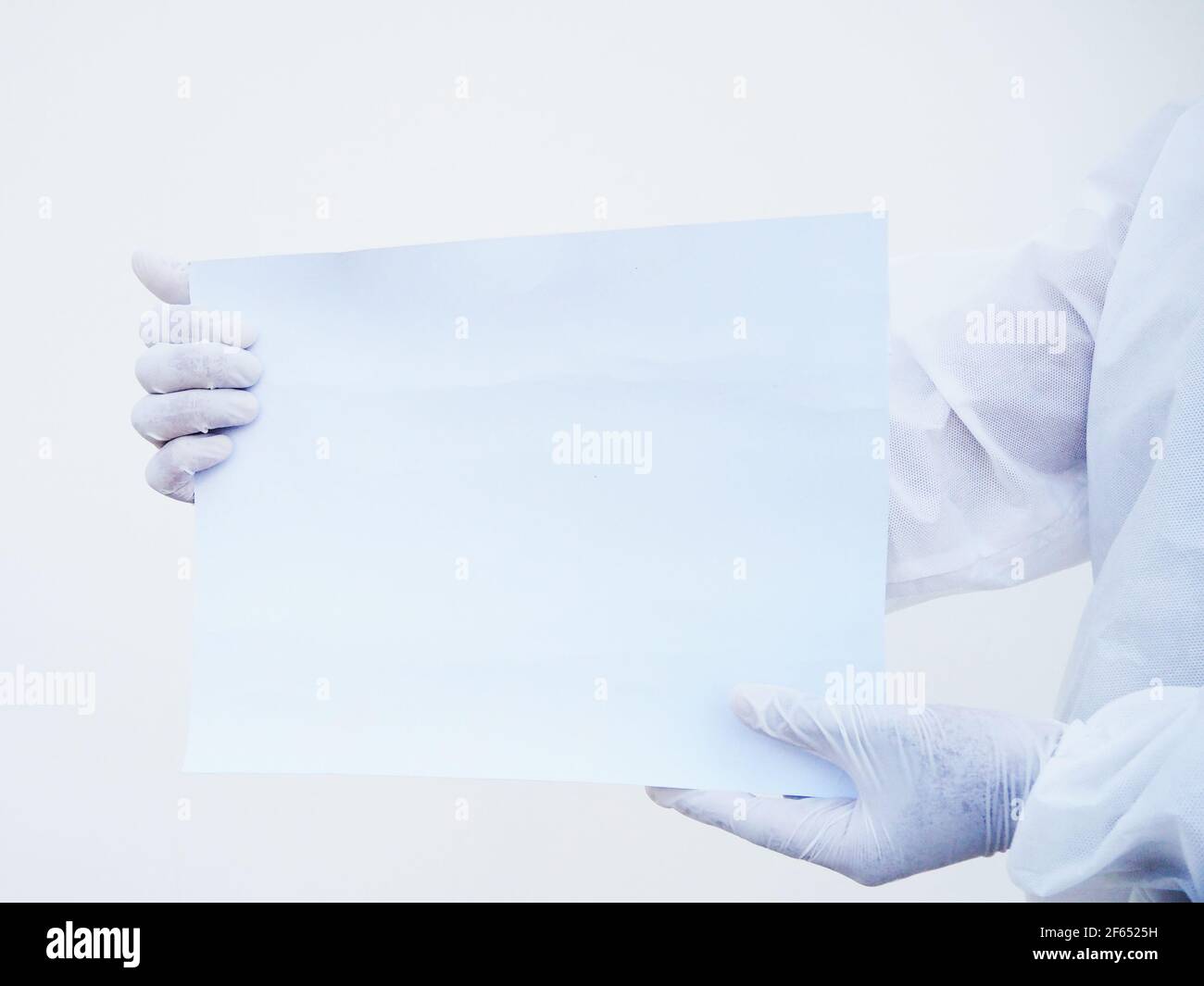 Closeup mani di medico o scienziato in uniforme DPI suite tenendo carta bianca per il testo con entrambe le mani mentre si guarda avanti. Coronavirus o COVID-19 co Foto Stock