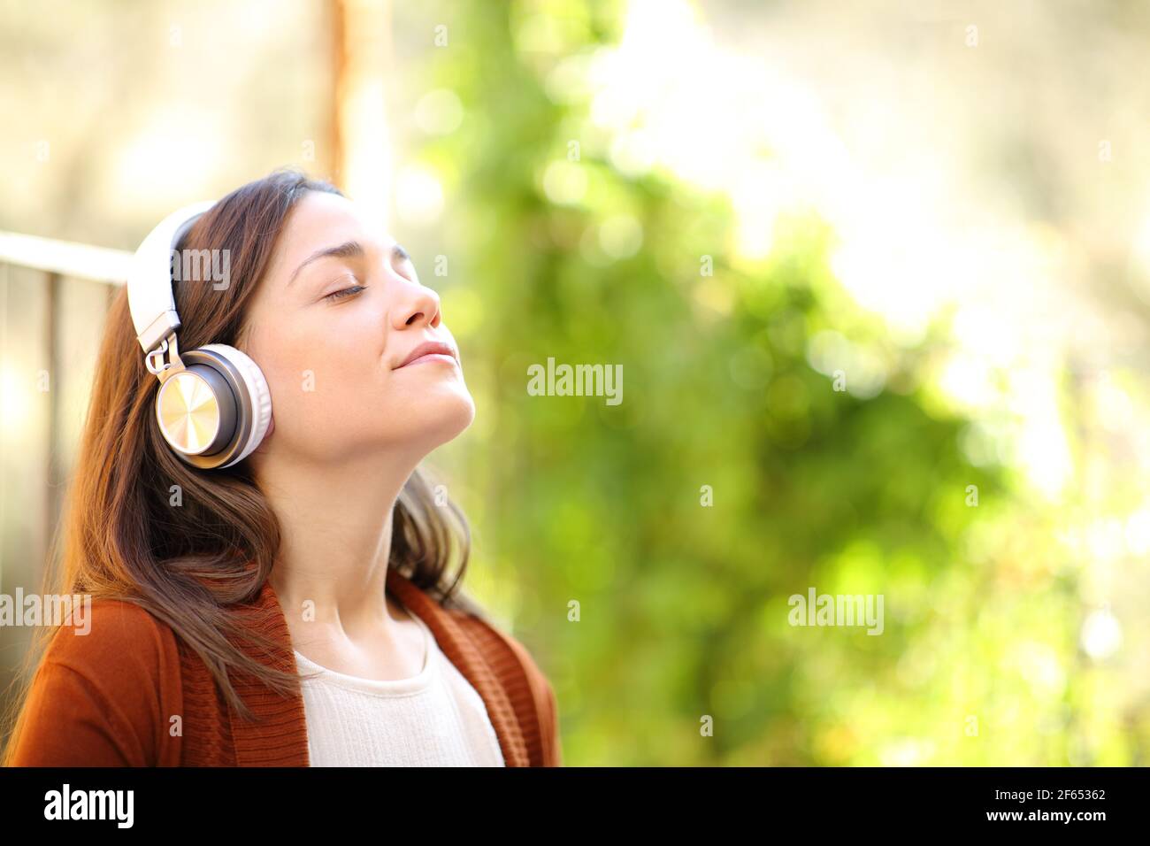 Donna rilassata che indossa cuffie che respirano aria fresca meditando l'ascolto musica in un giardino della casa Foto Stock