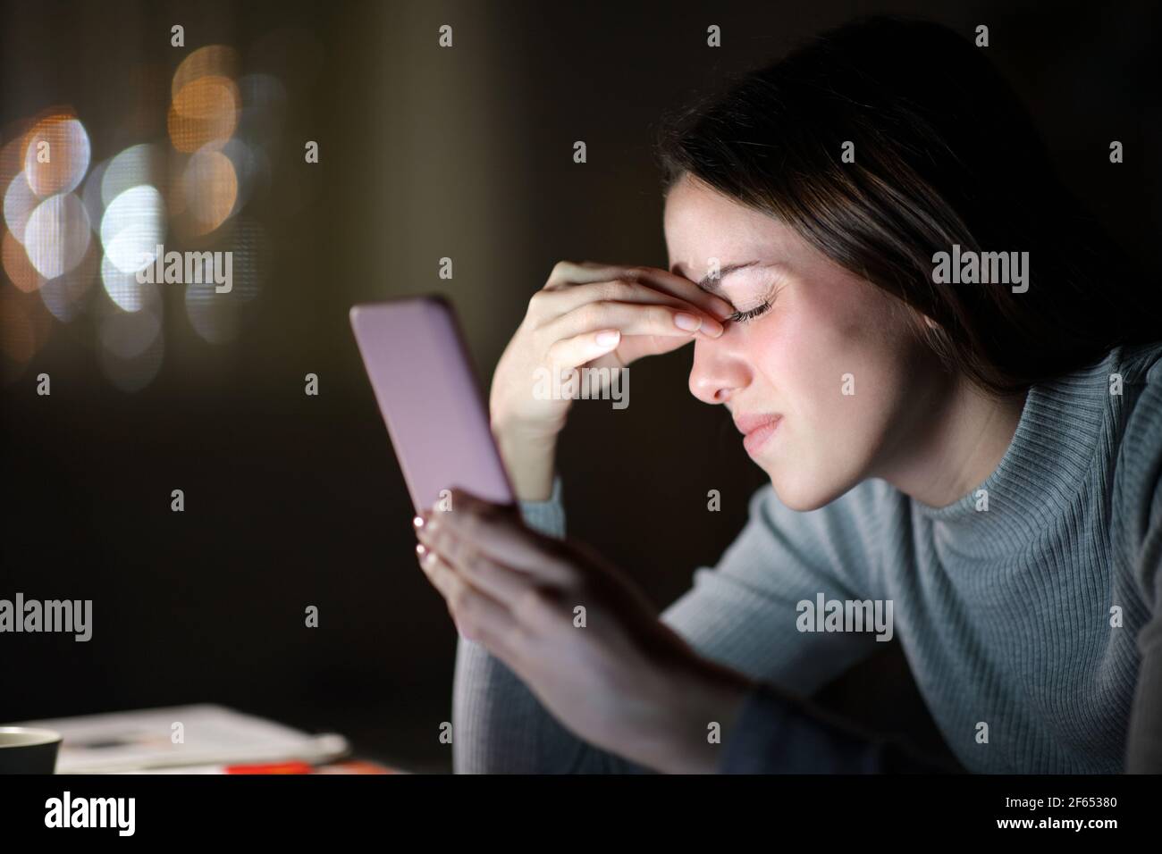 Donna stanca che soffre di affaticamento degli occhi utilizzando il telefono cellulare di notte a casa Foto Stock