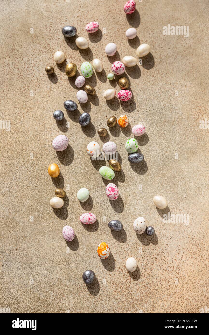 Uova multicolore a forma di caramelle su uno sfondo di cemento chiaro. Buona Pasqua. Concetto di minimalismo. Messa a fuoco selettiva. Vista dall'alto. Foto Stock