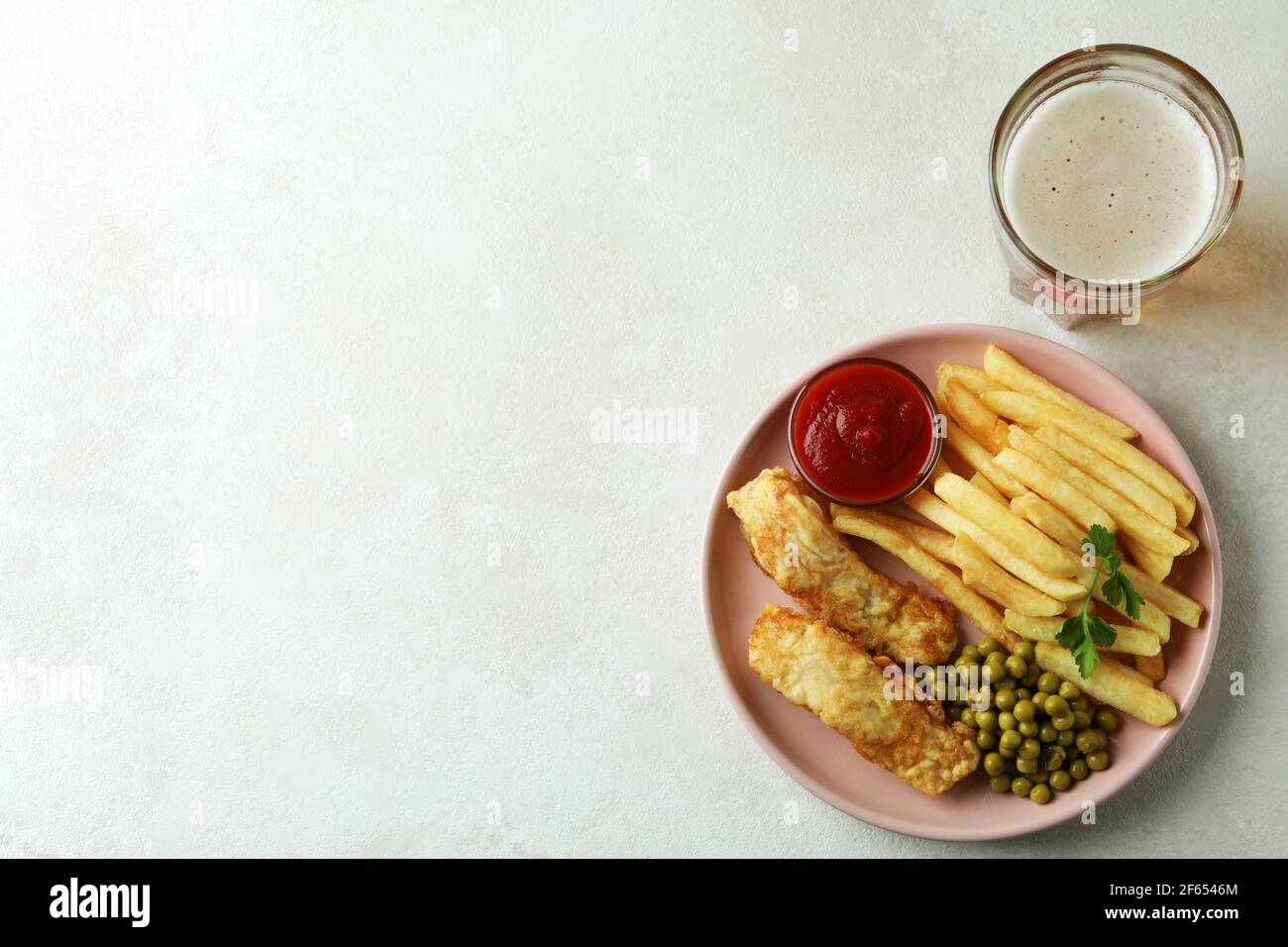 Piatto con pesce fritto e patatine e birra su tavola testurizzata bianca Foto Stock
