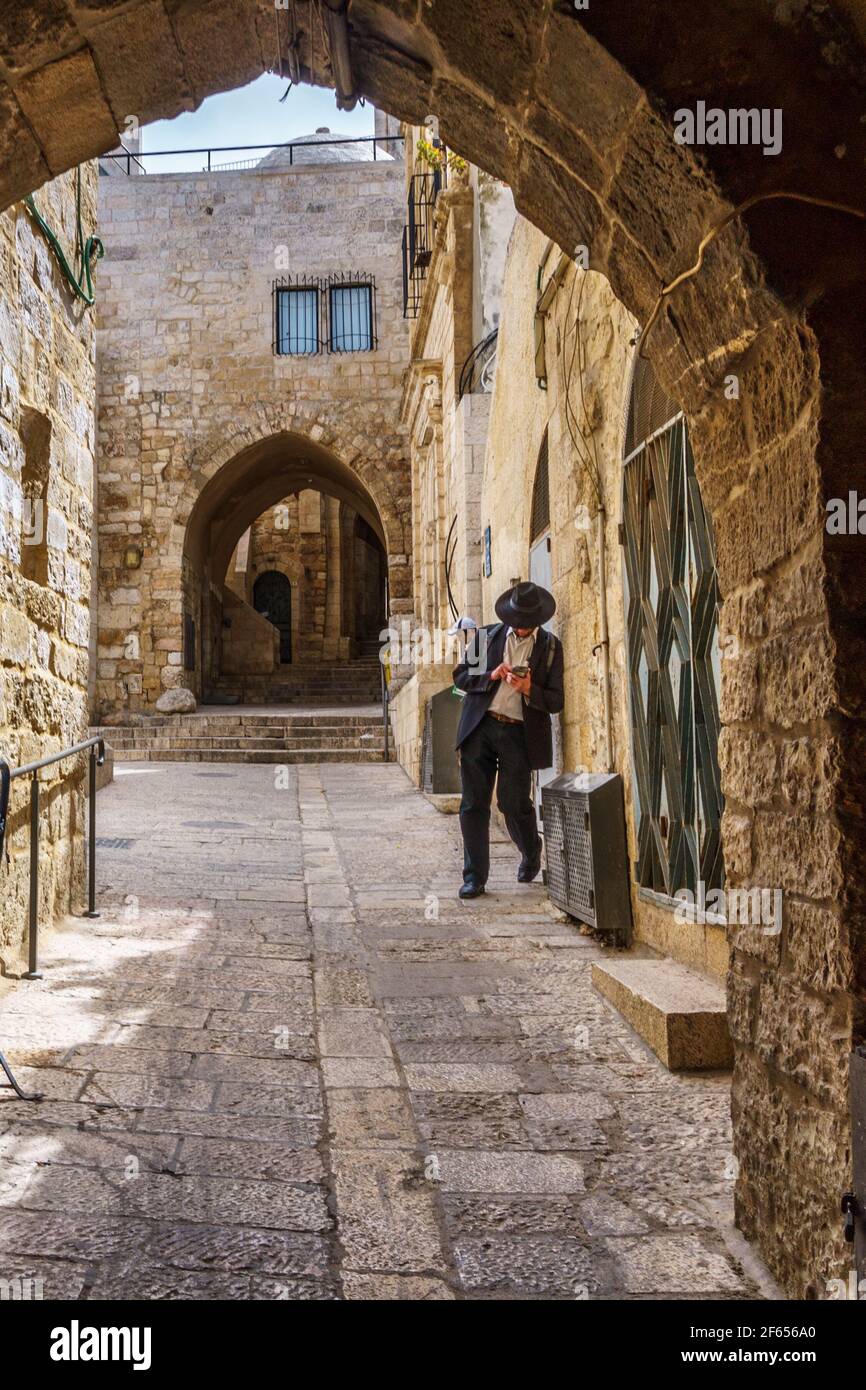 un uomo ortodosso in un cappello largo-brimmed sulla strada Della città vecchia di Gerusalemme guardando qualcosa in smartphone Foto Stock