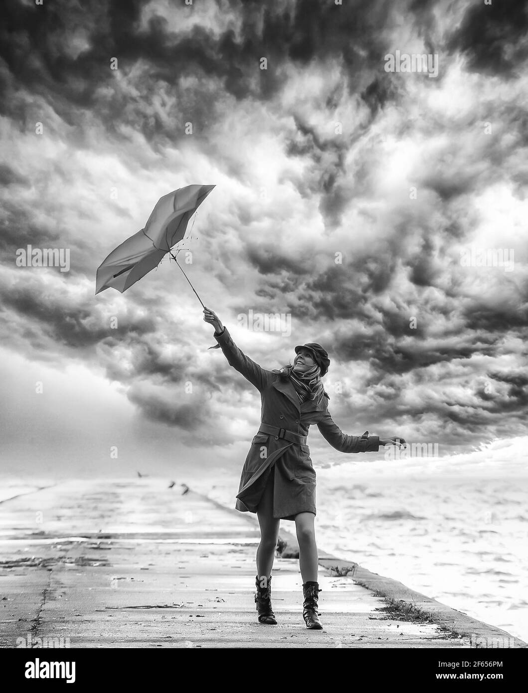 Una ragazza in camice arancione con ombrello in tempo tempestoso sul molo. Cielo nuvoloso. Bianco e nero. Foto Stock