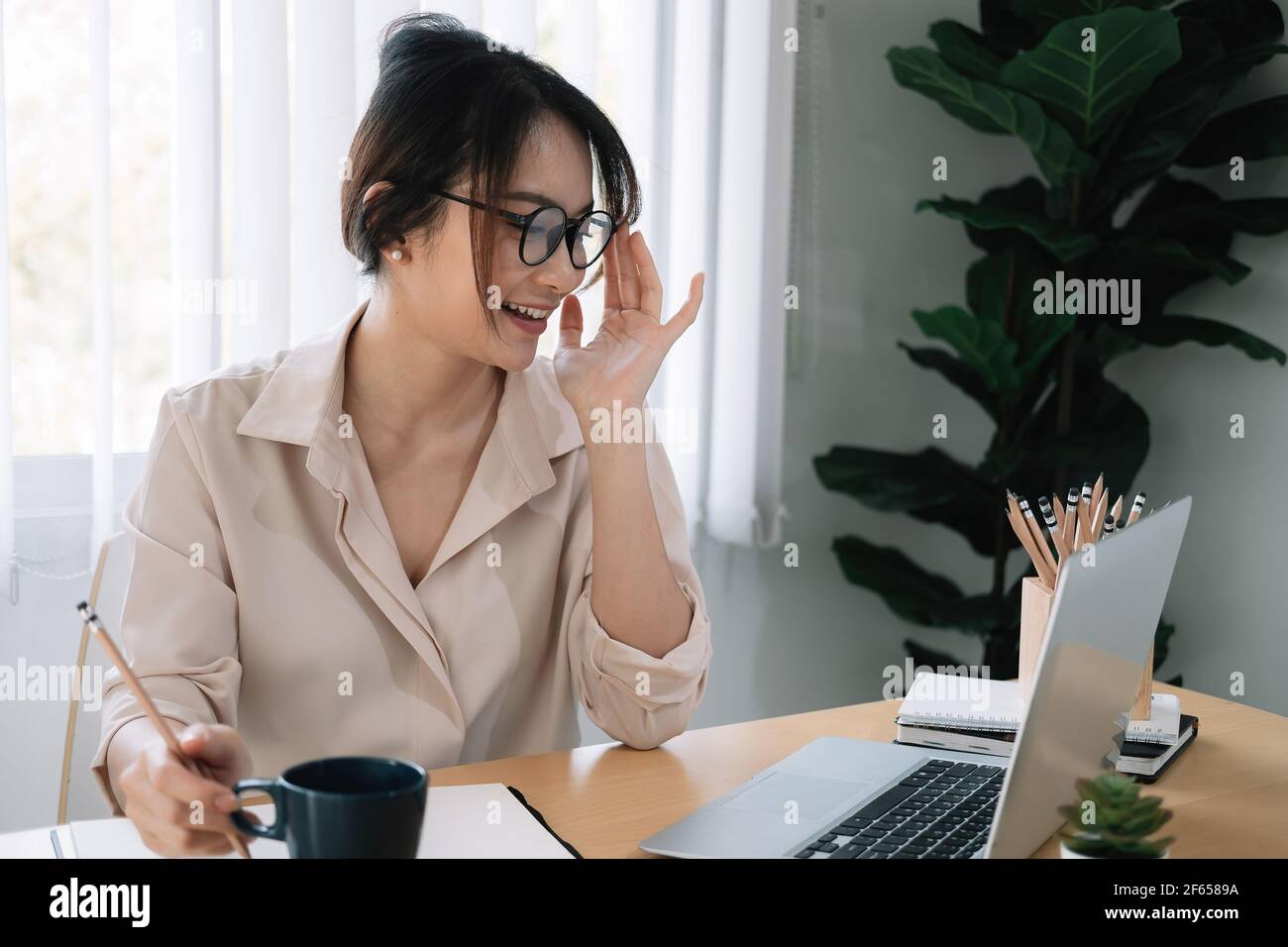 Giovane studentessa asiatica con occhiali studia con un computer portatile per l'apprendimento online a casa Foto Stock
