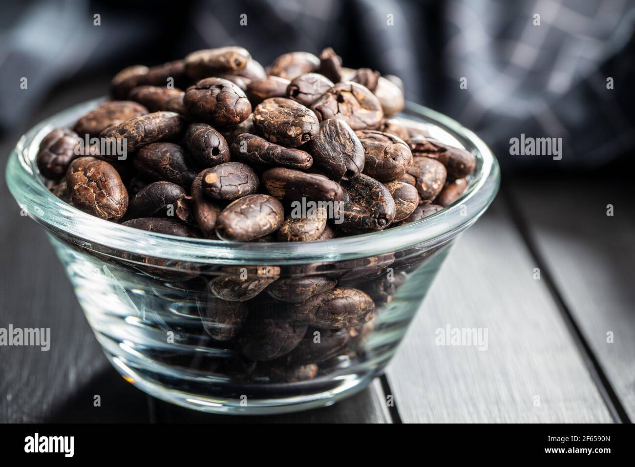 Fagioli di cacao arrostiti in recipiente di vetro su tavola nera. Foto Stock