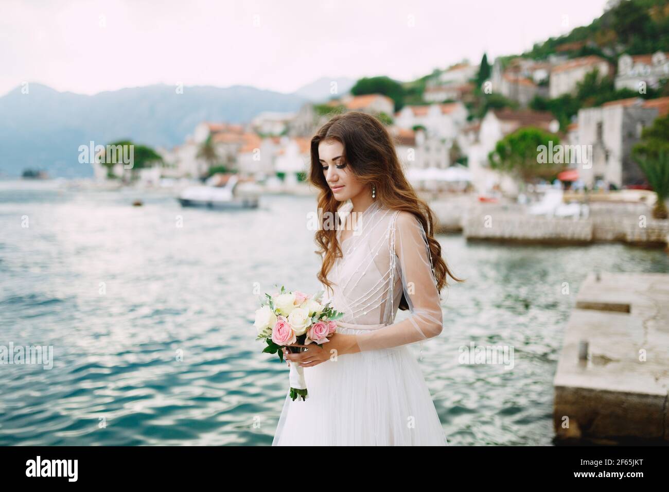 La sposa tiene in mano un bouquet di rose e si trova sul molo vicino alla città vecchia di Perast Foto Stock