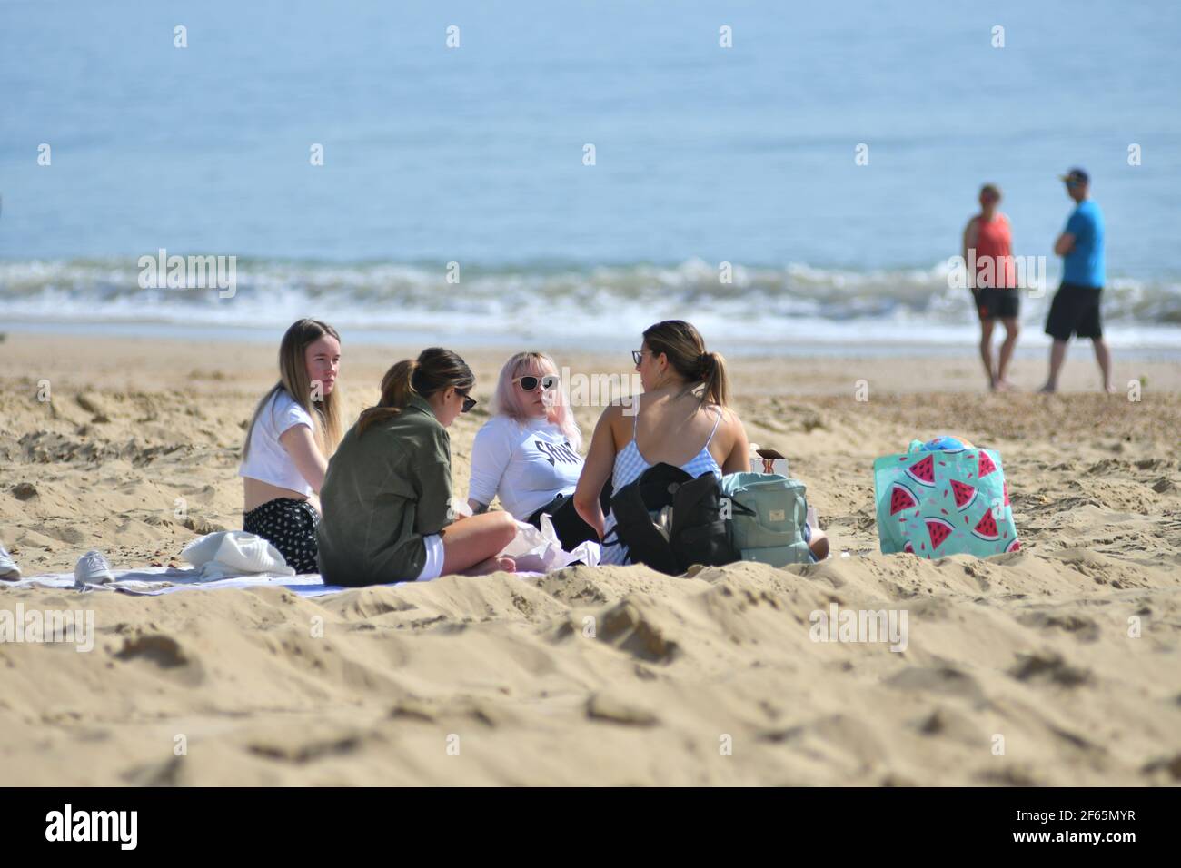 Boscombe, Bournemouth, Dorset, Regno Unito, 30 marzo 2021, Meteo. Un'ondata di caldo primaverile coincide con il rilassamento delle restrizioni del coronavirus che ora permettono a un massimo di sei persone di incontrarsi all'aperto. Le persone si dirigono verso la spiaggia, poiché le temperature si prevedono che raggiungano o superino i 20 gradi, diversi gradi al di sopra della media per la fine di marzo. Un gruppo di ragazze si siedono a parlare sulla spiaggia. Credit: Paul Biggins/Alamy Live News Foto Stock