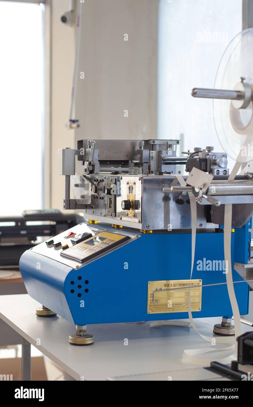 Vista laterale attrezzatura professionale sul tavolo in fabbrica, macchina da taglio a nastro elastico a freddo o a caldo cinese blu, tagliabasette raso per etichette o etichette Foto Stock