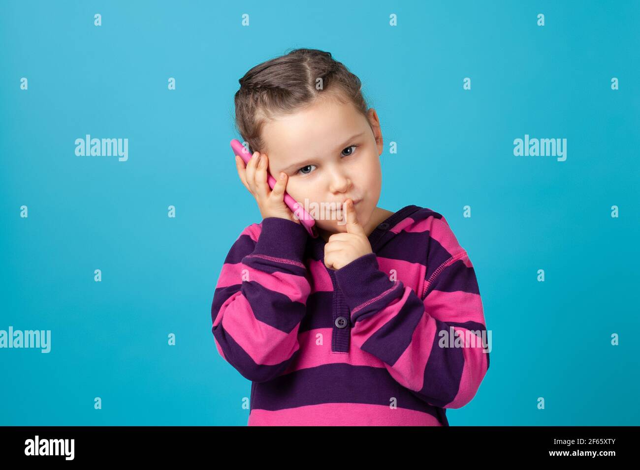 primo piano ritratto di una ragazza seria con pigtail che fa la telefonata, tenendo il dito alla bocca, segreto o richiesta di silenzio, isolato su sfondo blu Foto Stock