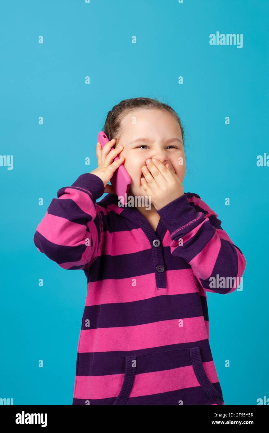 ritratto di ragazza con i pigtail ridendo a lacrime facendo la telefonata e coprendo la sua bocca con la mano da ridere, isolato su uno sfondo blu Foto Stock