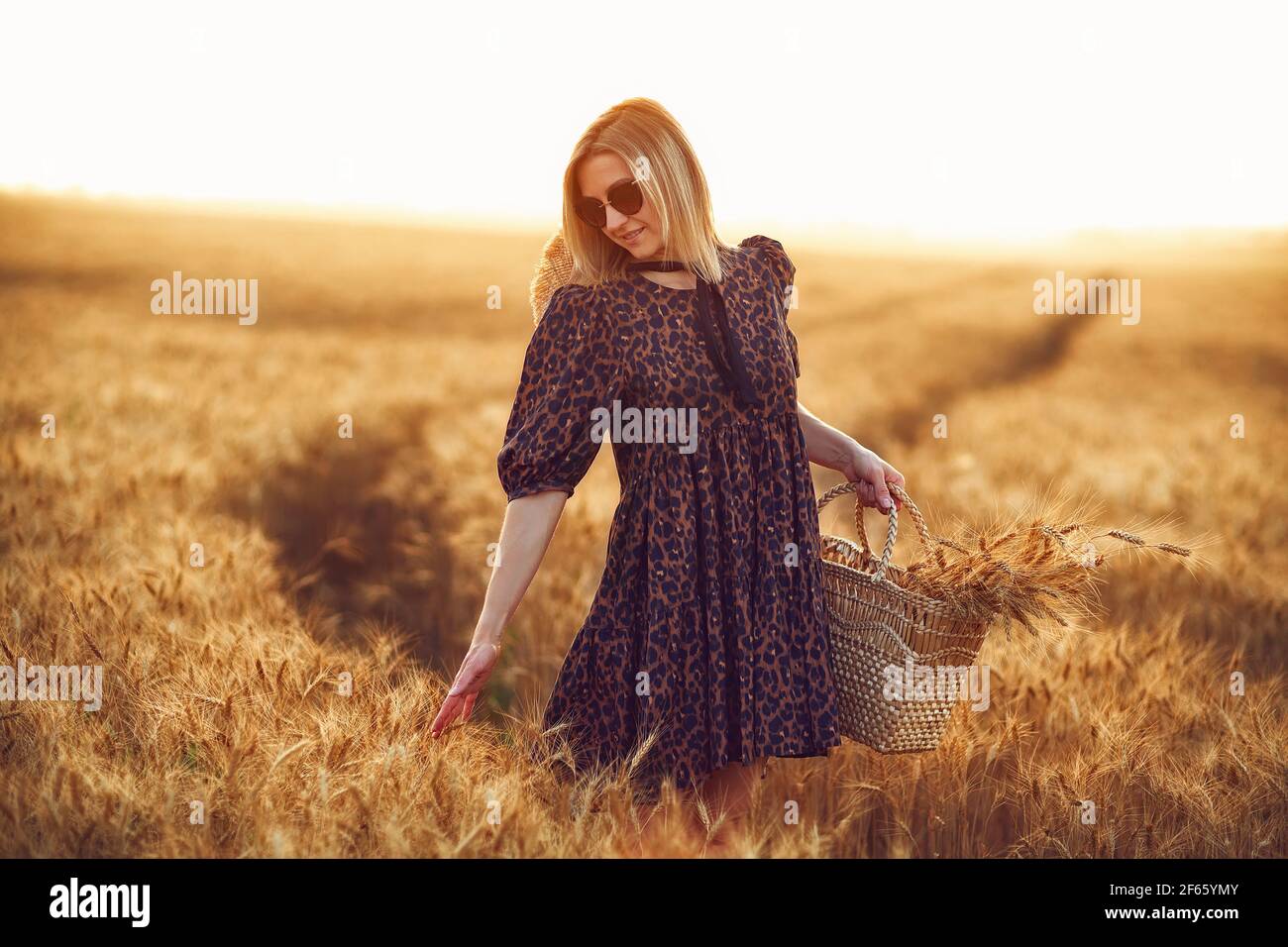 Donna in abito con stampa animale, cappello di paglia davanti al Sole nel mezzo Foto Stock