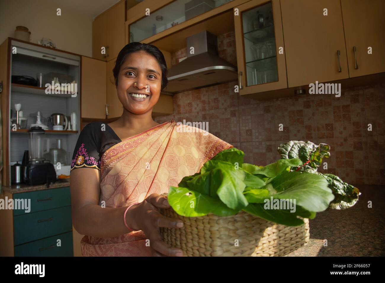 Una donna sorridente con verdure verdi a foglia coltivate in casa Foto Stock