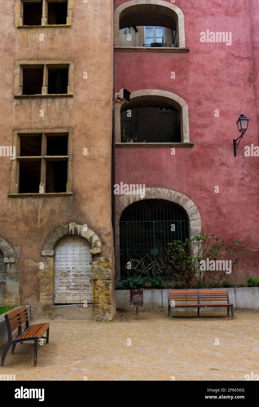 Panchine in un cortile nella Vecchia Lione, Francia; gli edifici dietro sono alti - uno rosa, uno arancione. Foto Stock