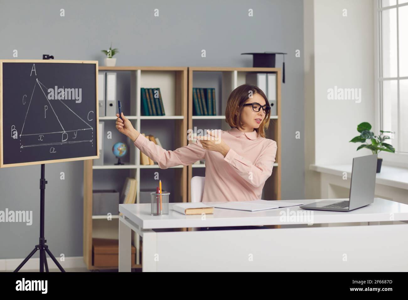 L'insegnante di matematica si siede in classe e spiega un nuovo argomento della lezione online con un laptop. Foto Stock