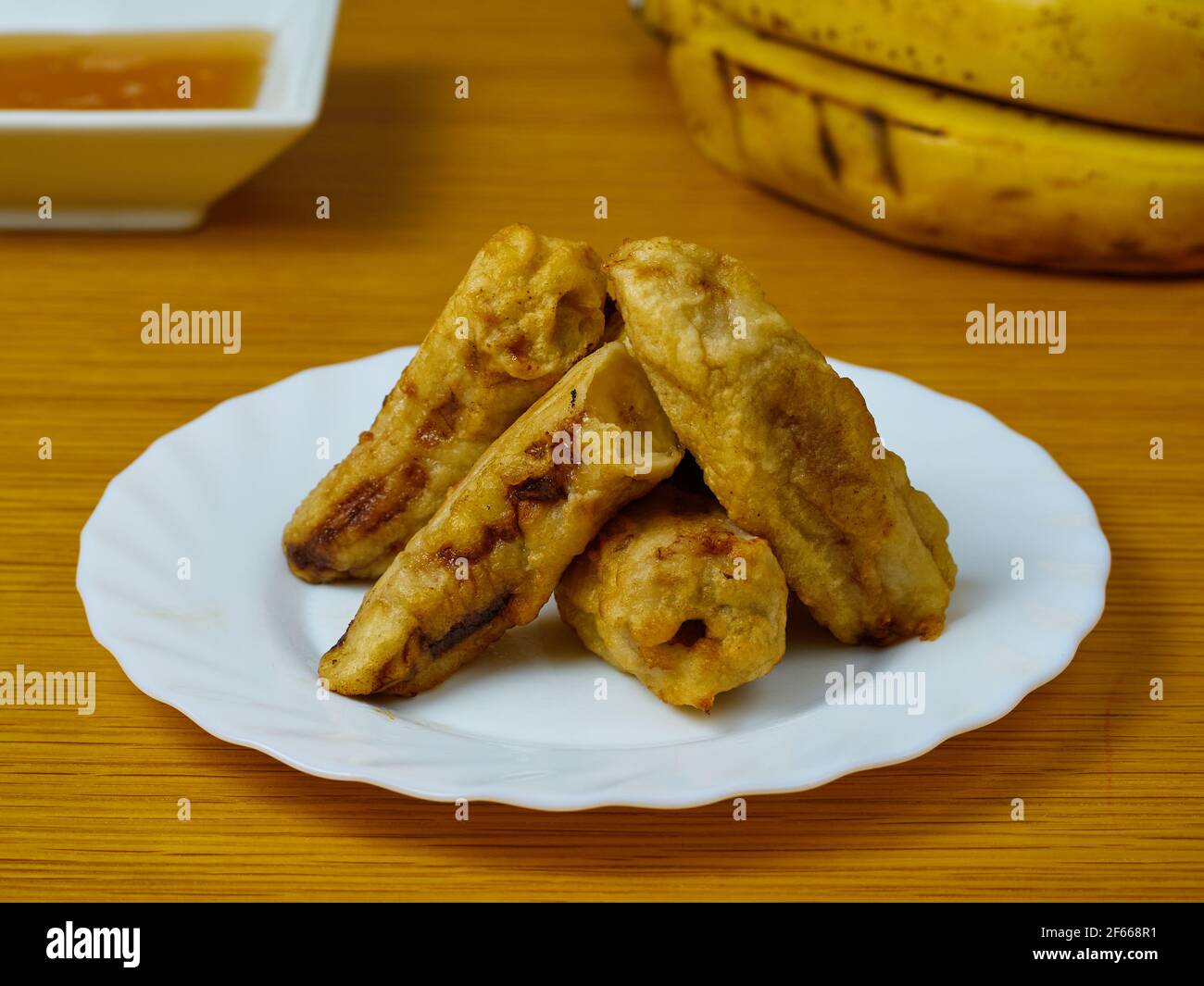 Fette fritte della plantana matura su un piatto bianco decorato con banane e miele Foto Stock