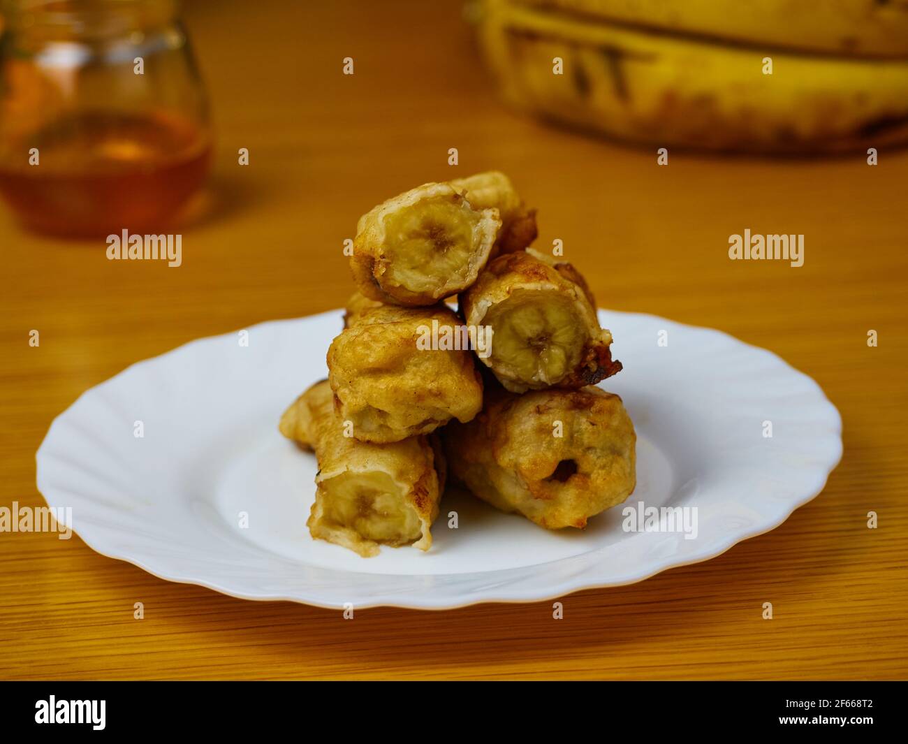 Fette fritte della plantana matura su un piatto bianco decorato con banane e miele Foto Stock