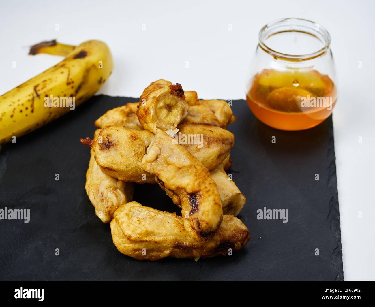 Fette fritte della pianta matura decorate con una banana e miele su una tavola di ardesia nera Foto Stock