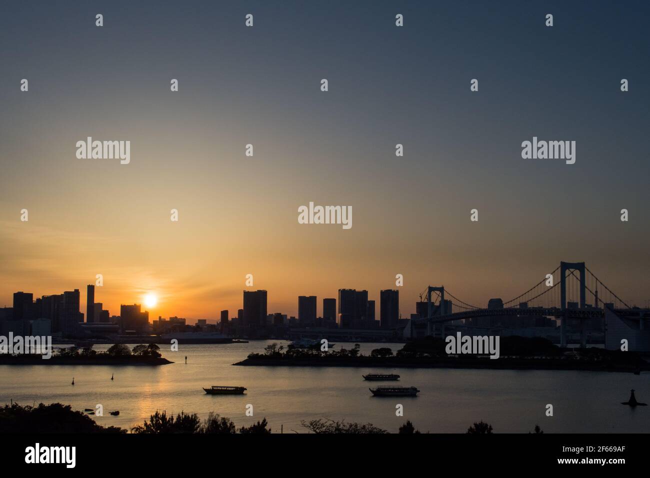 Tokyo, Giappone - il sole e la silhouette dello skyline di Tokyo e del Ponte dell'Arcobaleno, un ponte sospeso che attraversa la Baia di Tokyo settentrionale. Foto Stock