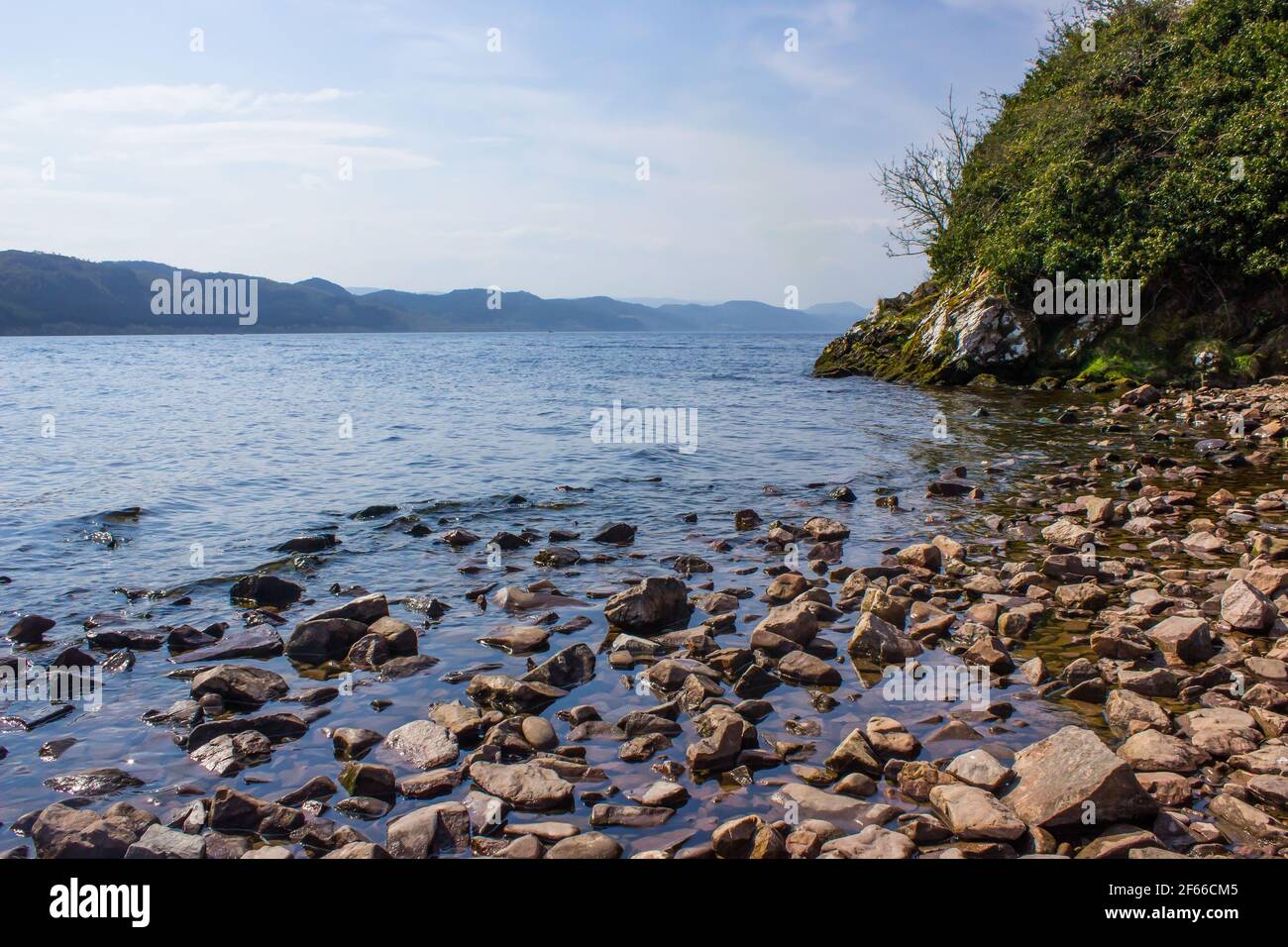 Massi ai margini di Loch Ness, Scozia, in una giornata di sole e limpida, con le montagne visibili sulla riva opposta Foto Stock