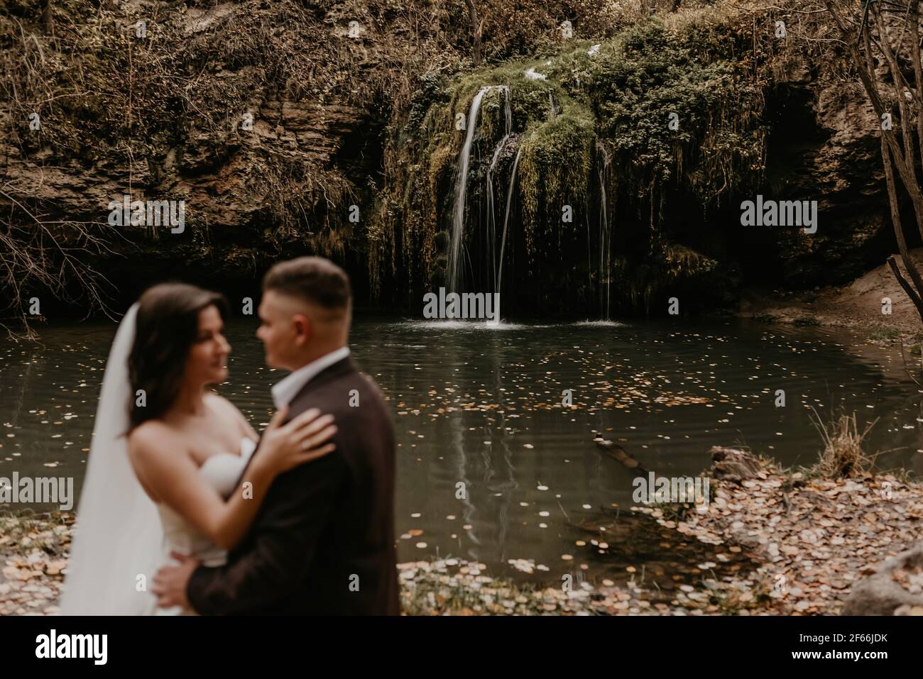 coppia fuori fuoco. sposa skinny in abito da sposa bianco e lungo velo abbracci sposare in un vestito. piccolo stagno lago fiume. estate-autunno tramonto arancione caduto Foto Stock