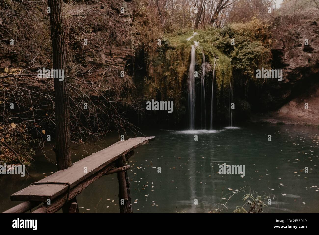 Molo in legno. Piccolo stagno lago fiume verde. Estate-autunno dopo il tramonto caduta foglie d'arancio nebbia. Cascata Burbun nel villaggio di Lys Dunaivtsi Foto Stock