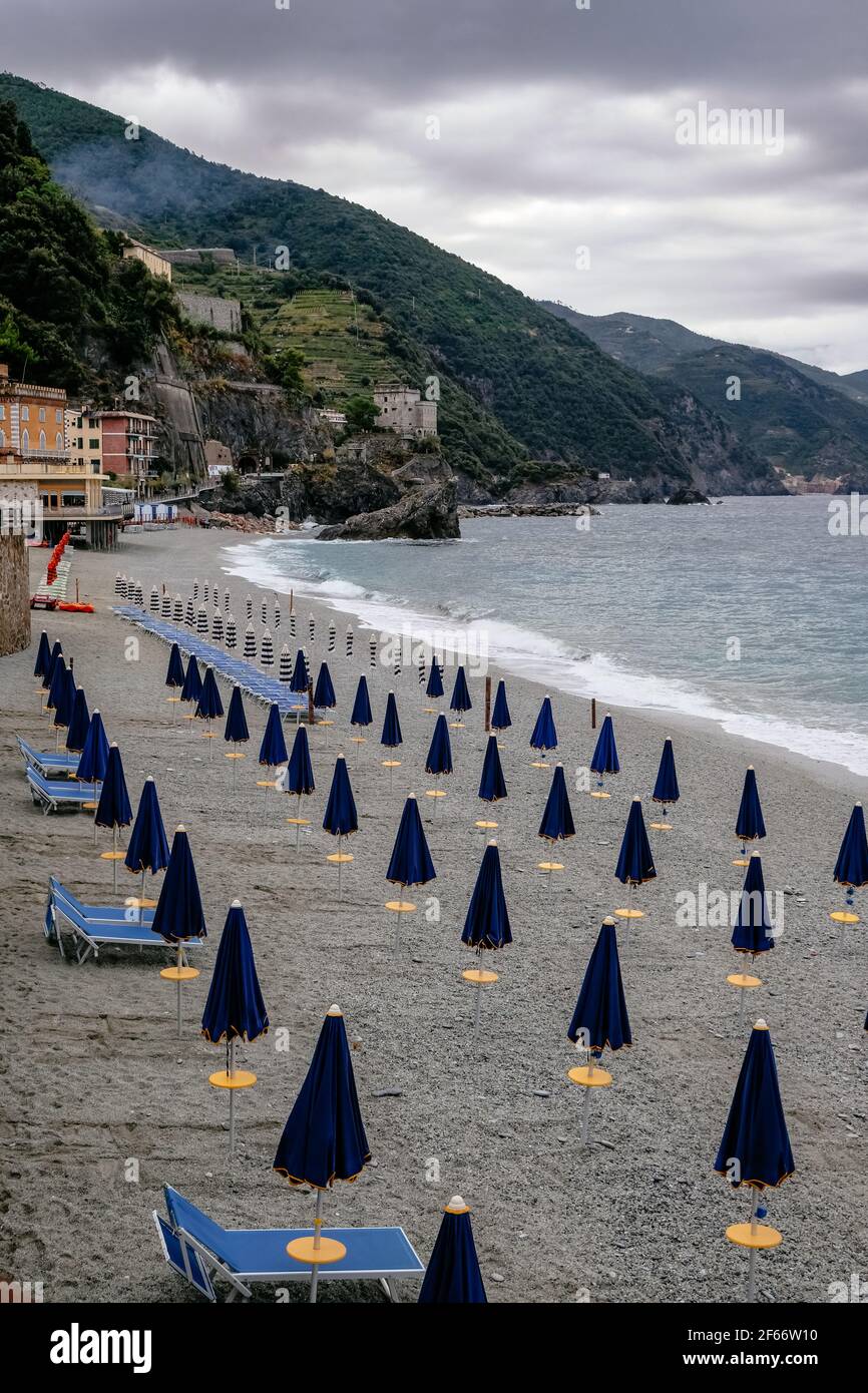 Ombrelloni chiusi in un'immacolata spiaggia di Pebble con splendide acque cristalline - Monterosso al Mare, cinque Terre, Italia Foto Stock