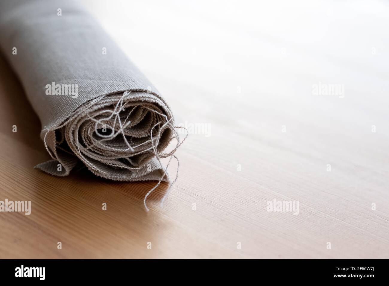 Rotolo di tessuto di lino naturale con fili sporgenti su a. tavolo di legno Foto Stock