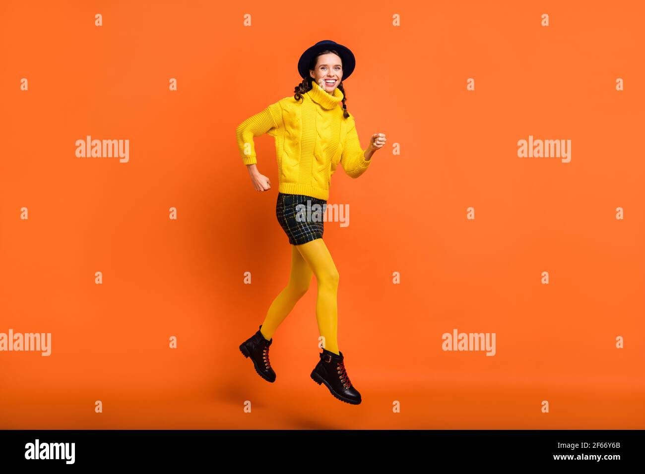 Vista completa del corpo di una bella ragazza allegra e skinny azione di corsa di salto isolata su sfondo arancione luminoso Foto Stock