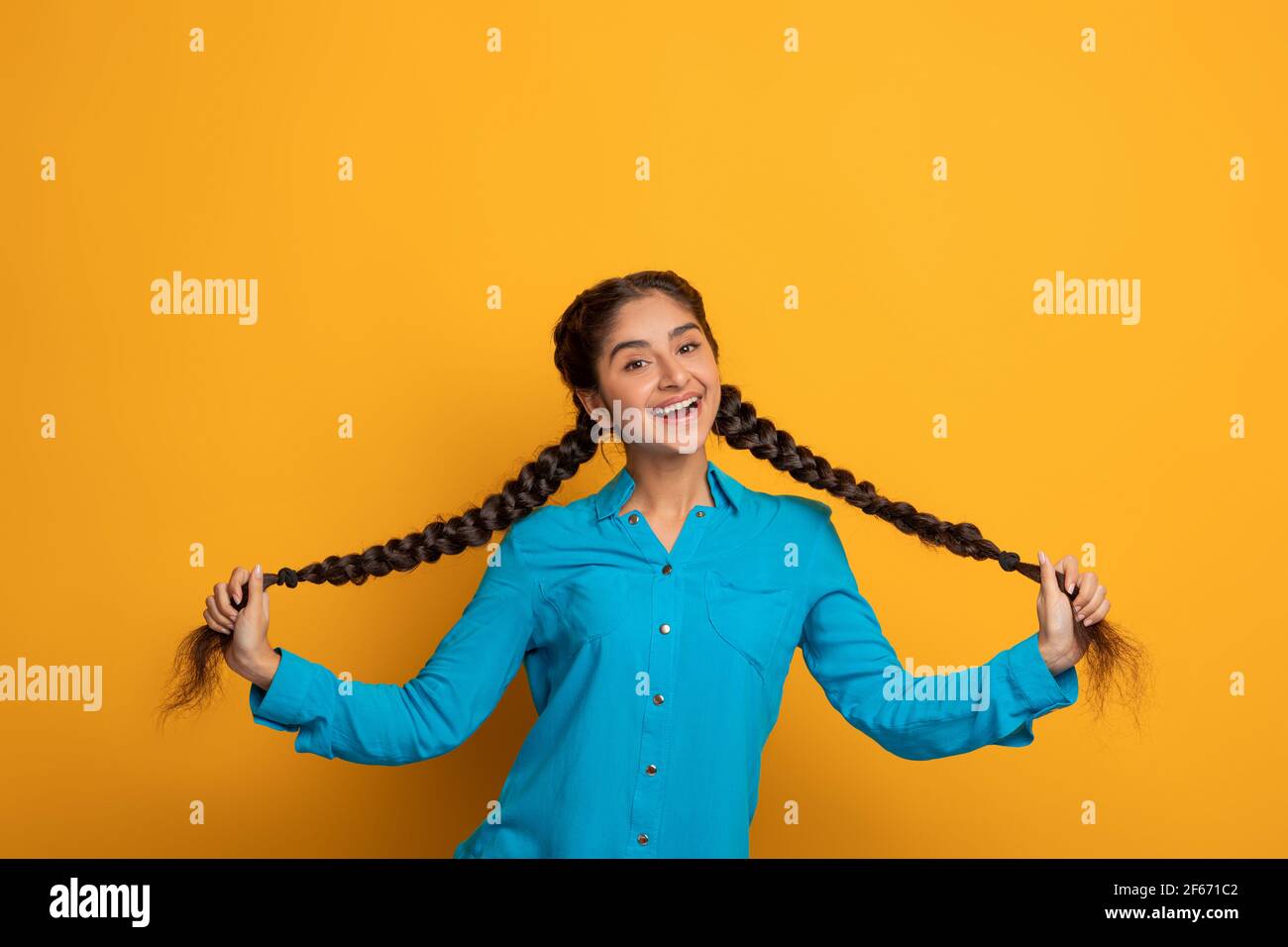 Felice donna indiana che tiene e tirando le sue due lunghe trecce Foto Stock