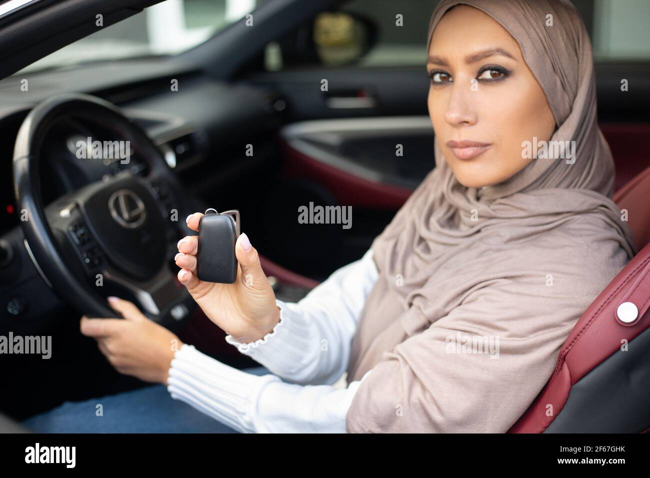 Donna musulmana fiduciosa che mostra le chiavi automatiche, seduto sul sedile del conducente Foto Stock