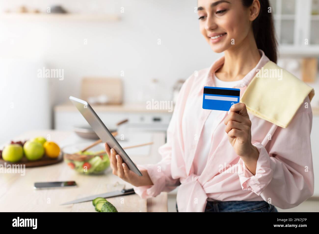 Donna che acquista online utilizzando tablet e carta di credito in cucina Foto Stock