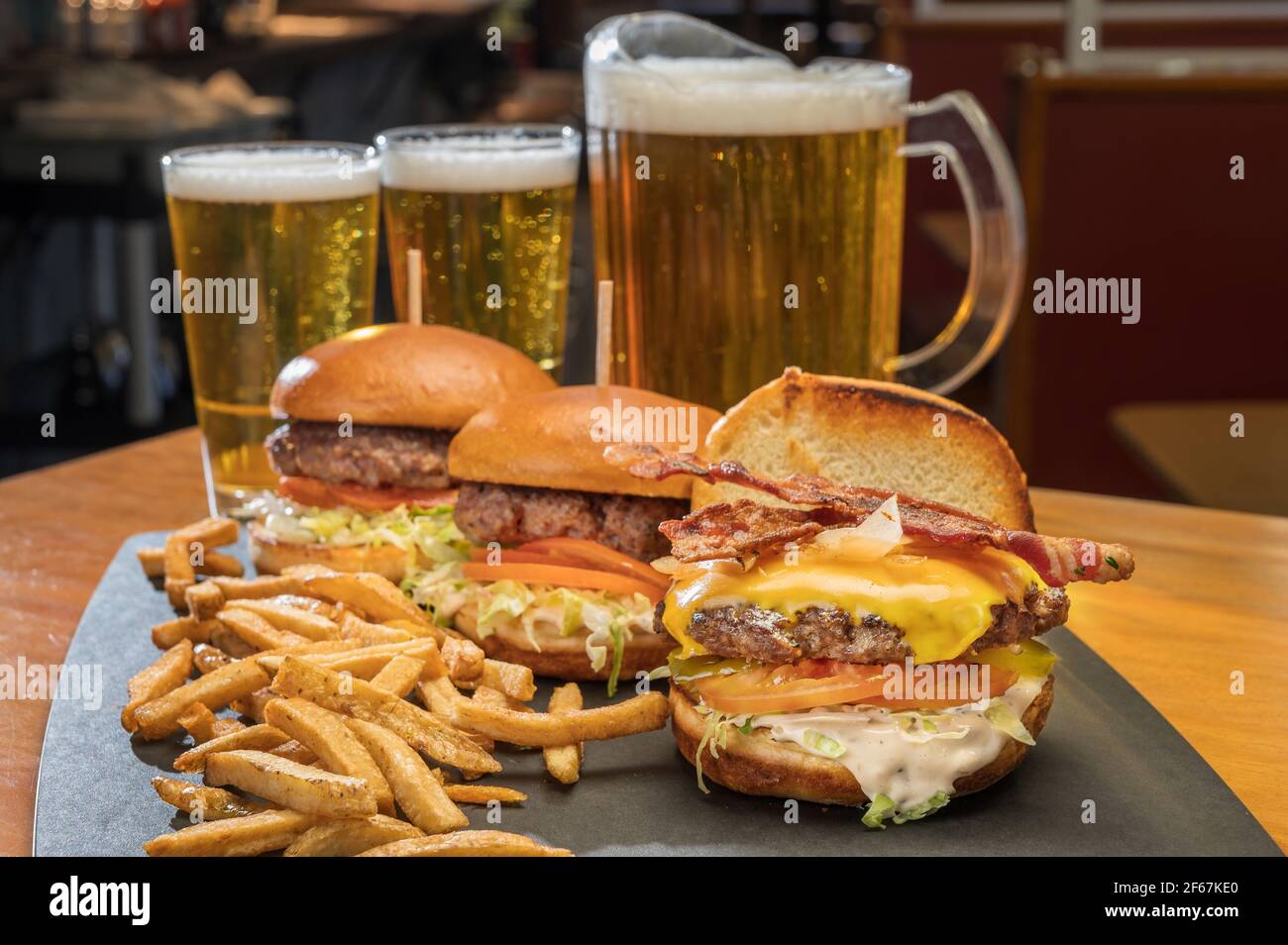 Piatto di hamburger con formaggio bacon con patatine fritte in un ristorante in stile cena con una brocca di birra. Foto Stock