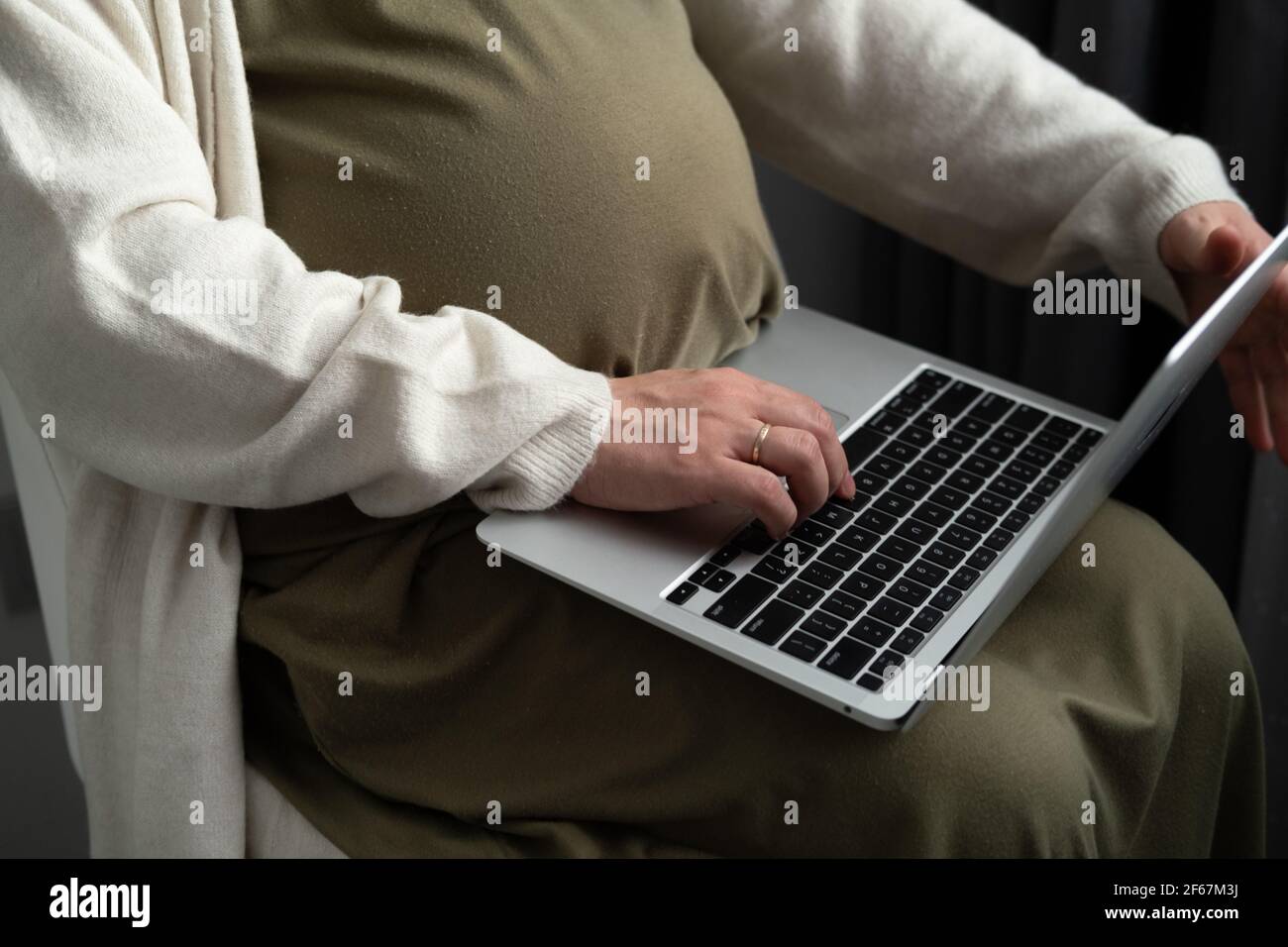 Attraente giovane donna incinta che lavora a distanza online da casa. Primo piano le mani della donna sul computer portatile con la gravidanza avanzata del ventre grande Foto Stock