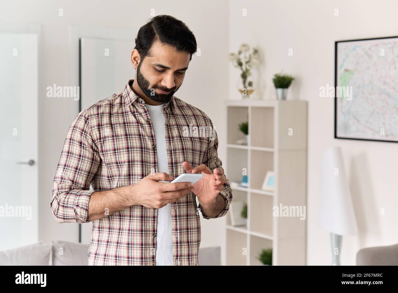 Giovane uomo indiano che tiene uno smartphone utilizzando il telefono cellulare a casa. Foto Stock