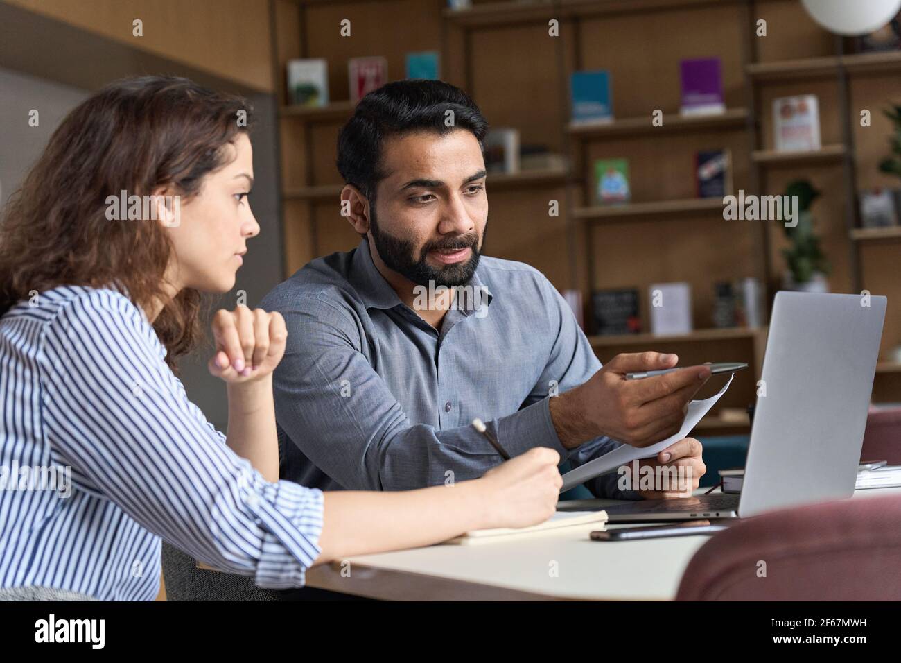 Insegnante o mentore indiano che aiuta lo studente latino, insegnando intern usando il laptop. Foto Stock
