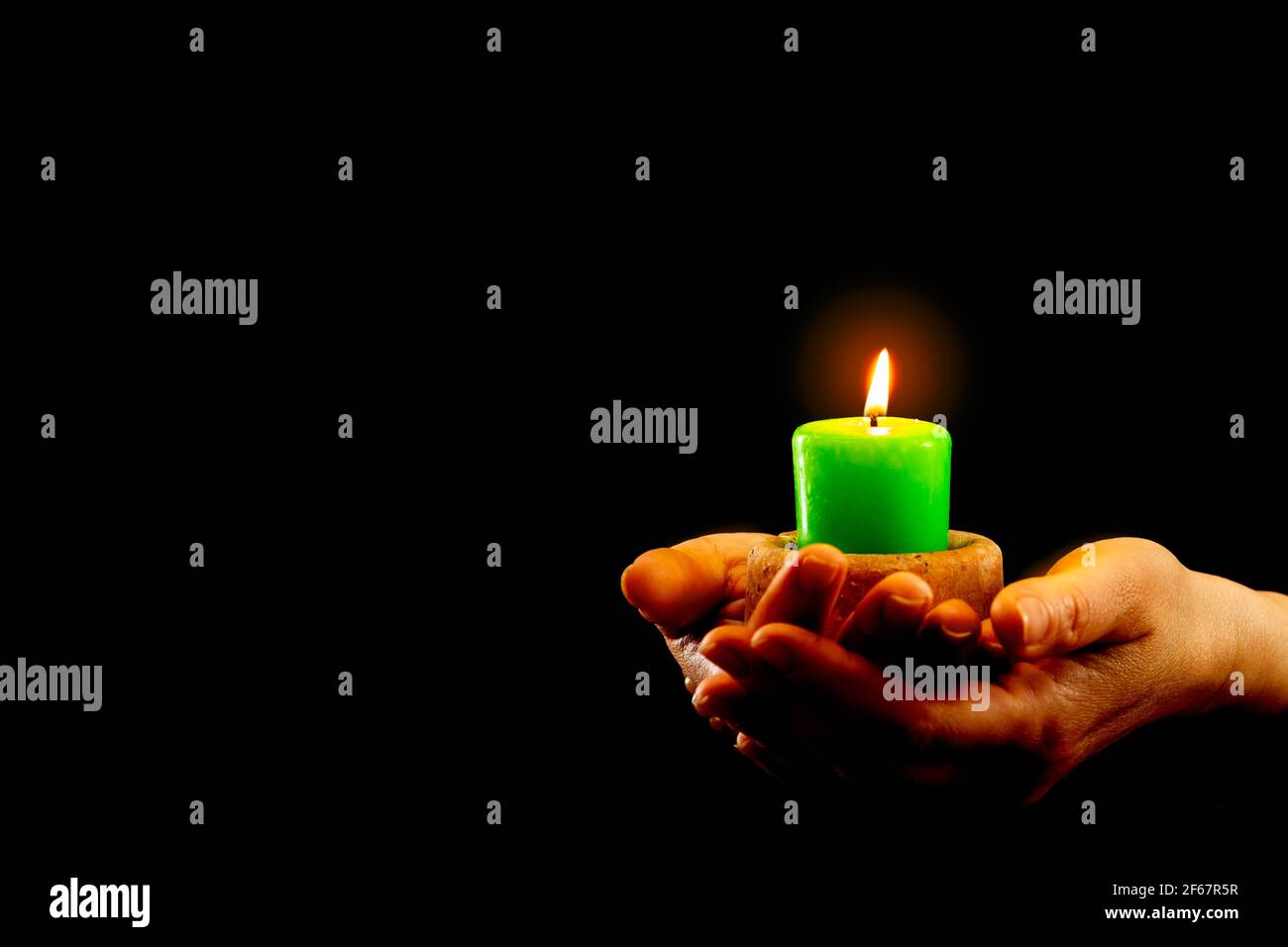 Le mani tengono la candela verde che brucia al buio. Foto Stock