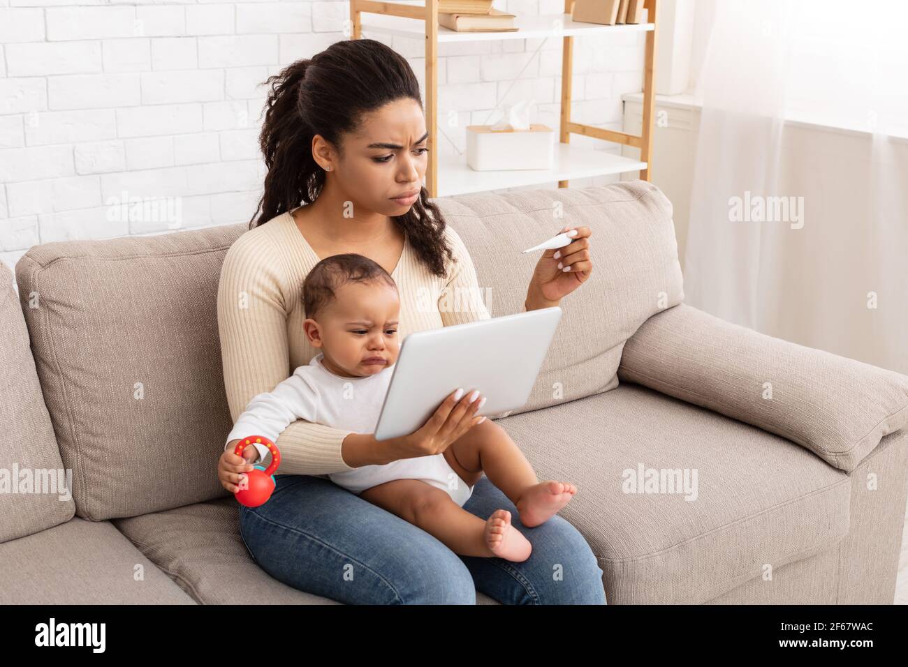 Frustrato mamma africana con il bambino malato usando la tavoletta a casa Foto Stock